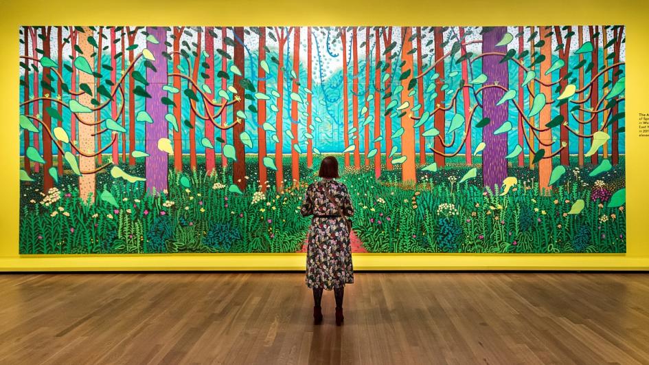 A woman looks at a painting of a path running through a forest in full bloom